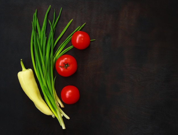 Gemüse liegt auf einem dunkelbraunen Holztisch Draufsicht Frühlingszwiebeln gelbe Paprika und reife rote Tomaten Konzept für gesunde Ernährung