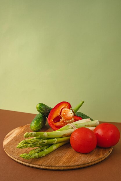 Gemüse liegt auf einem Holzbrett Tomaten Spargel Gurken rote Paprika braun hellgrüner Hintergrund Platz für Text