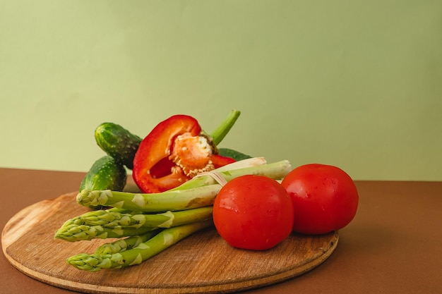 Foto gemüse liegt auf einem holzbrett tomaten spargel gurken rote paprika braun hellgrüner hintergrund platz für text