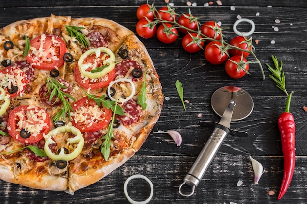 Gemüse-, Pilz- und Tomatenpizza auf einem schwarzen hölzernen Hintergrund. Es kann als Hintergrund verwendet werden
