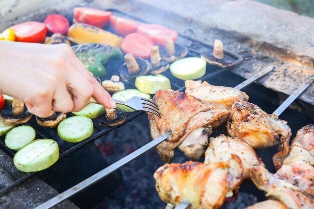 Gemüse und Fleisch auf dem Grill. Paprika, Tomaten, Champignons und Zucchini-Kürbis. Huhn auf offenem Feuer. Grillparty im Sommer. Gesundes natürliches Essen.