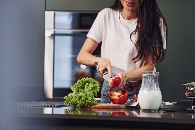 Gemüse und Milch auf dem Tisch Essen zubereiten Junge schöne Brünette in Freizeitkleidung drinnen in der Küche tagsüber