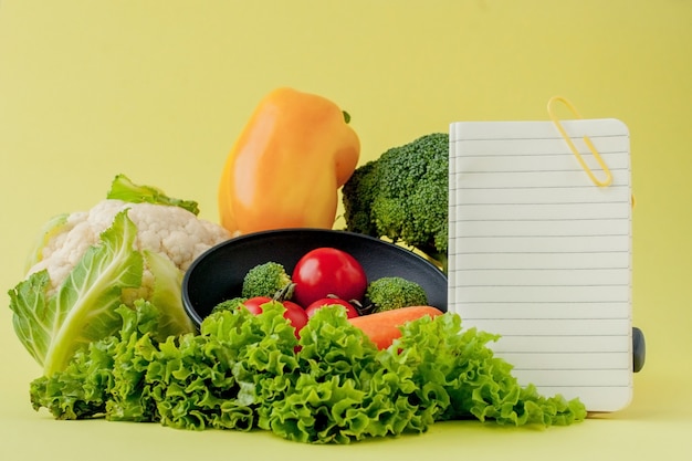 Gemüse und Notizbuch mit Kopierraum an der gelben Wand. Bio Gesundes Essen, Bio-Gemüse an der gelben Wand