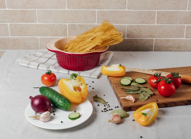 Gemüse und rohe Nudeln auf einem Tisch Kirschtomaten, gelbe Paprika, Gurke, rote Zwiebel