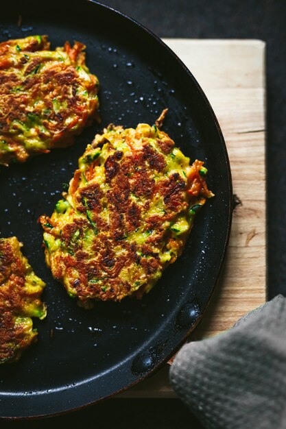 Gemüse Zucchini und Karottenkrapfen auf einer Pfanne und einem hölzernen Schneidebrett, Nahaufnahme von oben