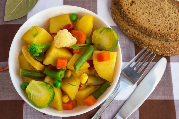 Gemüseeintopf (Kartoffeln, Spargel, Karotten, Rosenkohl, Mais, Erbsen, Wirsing, Brokkoli) in einer weißen Schüssel. Vegan.