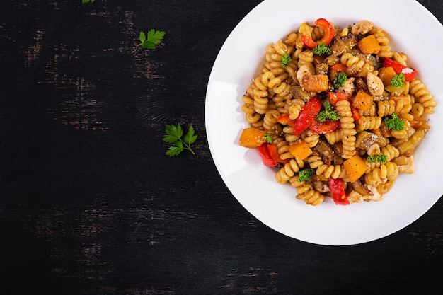 Gemüsenudeln fusilli corti bucati mit Auberginenpaprika und Hähnchen in weißer Platte auf dunklem Tisch Draufsicht