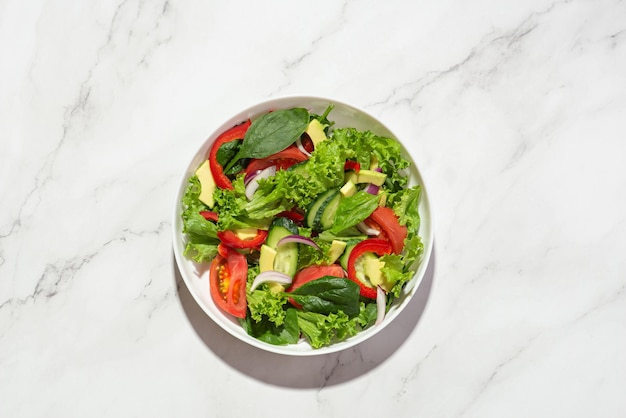 Gemüsesalat mit Avocado in einem weißen Teller auf grauem Hintergrund