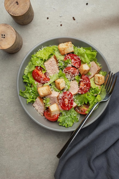 Gemüsesalat mit Hühnchen und Käse auf einem grauen Tisch. Caesar-Salat auf einem grauen Teller