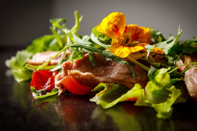 Gemüsesalat mit Schweinefleisch auf einem dunklen Teller.