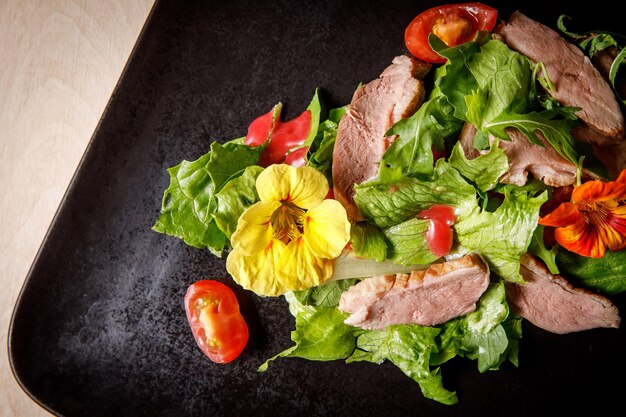 Gemüsesalat mit Schweinefleisch auf einem dunklen Teller.