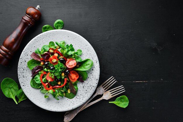 Gemüsesalat mit Spinat, Tomaten, Paprika und Kürbiskernen in einem Teller auf Holzhintergrund Draufsicht Freier Platz für Ihren Text Flach lag