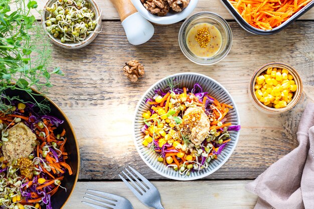 Gemüsesalat von frischem Rotkohl mit Karotten, Zwiebeln, Mais, Mungosämlingen in einem Teller auf hölzernem Hintergrund. Selektiver Fokus. Draufsicht.