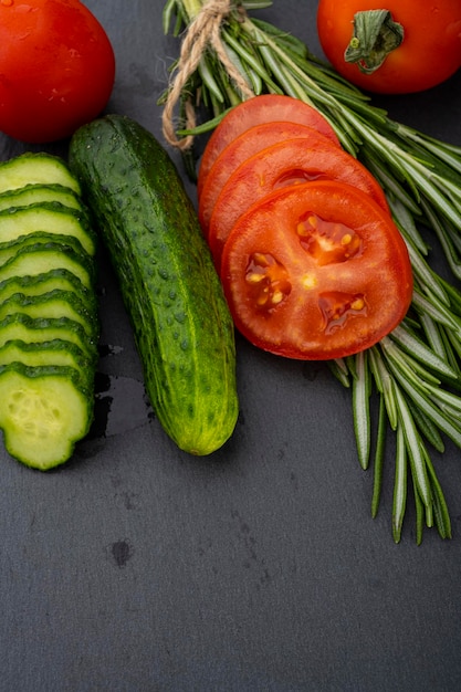 Gemüsetisch. Gurken, Tomaten und Rosmarin auf einem schwarzen Tisch