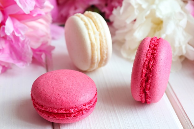 Gemütliche Bäckerei und floraler Hintergrund Macarons und Pfingstrosen Nahaufnahme auf einem weißen Holztisch