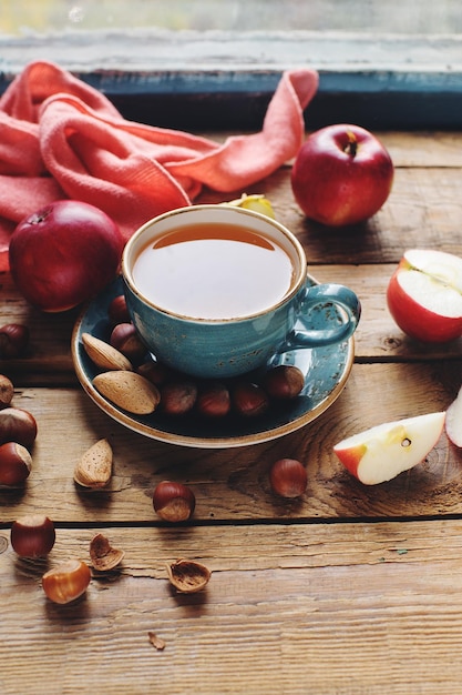 Gemütliche Herbstkomposition am Morgen mit Tasse Tee, frischen Äpfeln und Nüssen auf rustikalem Holztisch