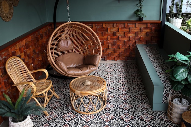 Gemütliche kleine Terrasse mit Hängesesseltisch aus Korbgeflecht und Holzstuhl auf dem Boden mit Blumenmuster
