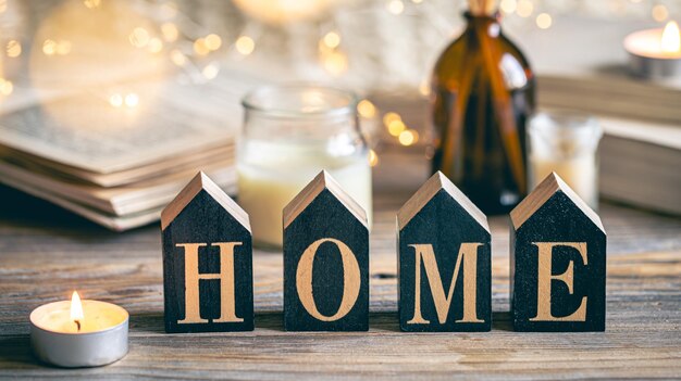 Gemütliche Komposition mit Holzwort Home und Kerzen auf einem verschwommenen Hintergrund mit Büchern und Bokeh-Lichtern