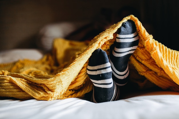 Gemütliche Position des Fußes in warmen Socken unter den Decken auf dem Bett