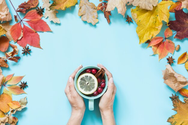 Gemütliche Tasse Getränk mit Moosbeere in der weiblichen Hand und Fall verlässt herum auf Blau.