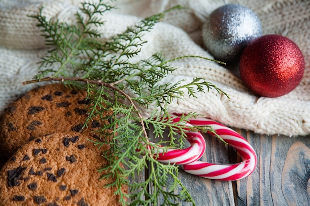 Gemütliche Weihnachtsdekoration. glänzende Kugeln auf gestrickter Texturdecke Schokoladenkekse gestreifte Zuckerstange und Wacholderzweige Hintergrund.