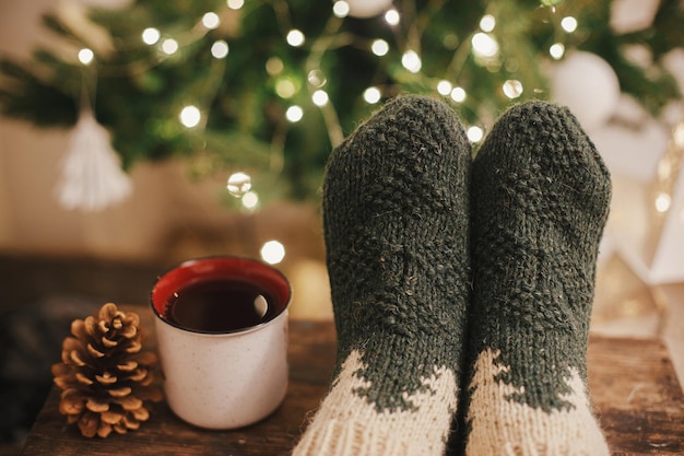 Gemütliche Wintermomente zu Hause Frauenfüße in kuscheligen Wollsocken und eine Tasse warmen Tee am Weihnachtsbaum