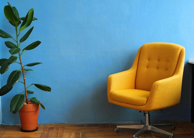 Gemütlicher Arbeitsplatz zu Hause Ein gelber Bürostuhl und ein Topf mit einer lebenden Pflanze stehen an einer blauen Wand