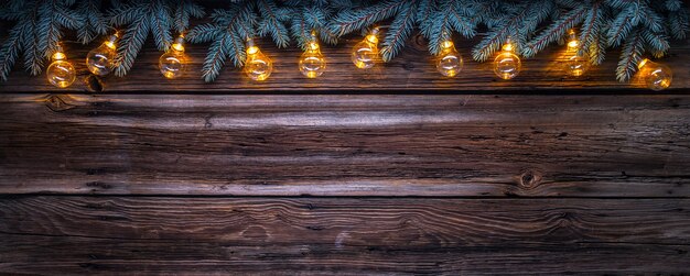 Gemütlicher Kopienraumhintergrund mit Fichtenzweigen und Weihnachtslichtern auf Scheunenholz