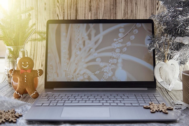 Gemütlicher Laptop-Bildschirm im Home Office und Lebkuchen in der Nähe von Weihnachtsbaum und flauschige, trendige Dekorationen Konzept der freiberuflichen Teilnahme an einem Webinar oder Anruf bei Freunden der Familie wegen der Sperrung des Virus