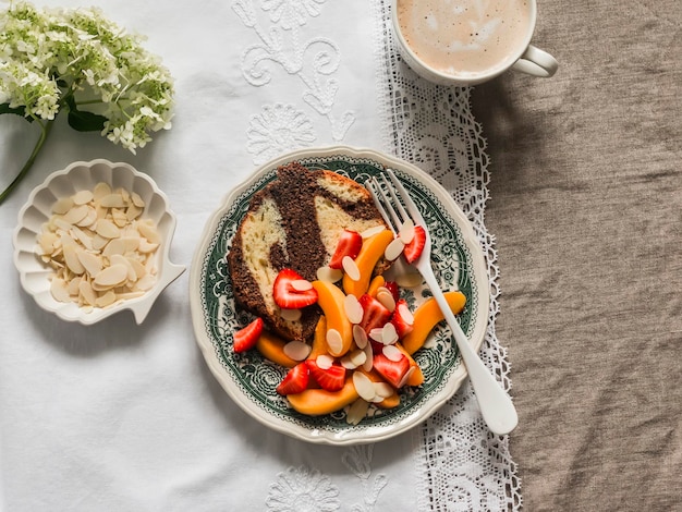 Gemütlicher Morgen-Cappuccino und Schokoladen-Cupcake, serviert mit Erdbeeren, Aprikosen und Mandelblüten auf der Tischplatte