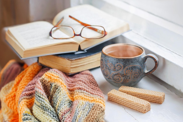 Gemütlicher Morgen zu Hause Eine Tasse Tee eine Decke alte Bücher und Gläser auf der Fensterbank