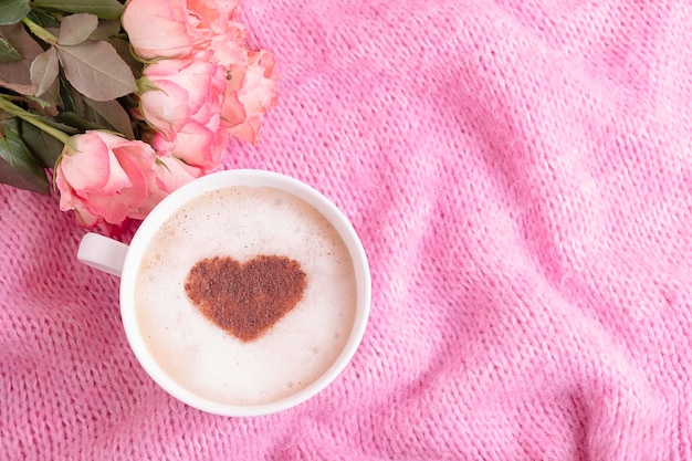 Gemütlicher romantischer Atmosphärenhintergrund mit gestrickten rosa Rosen und einer Tasse Kaffee mit Zimt ...