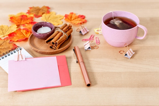 Gemütlicher Schreibtisch zu Hause mit Teetasse Herbstlaub Brief mit leerer Papierkarte auf Holzhintergrund