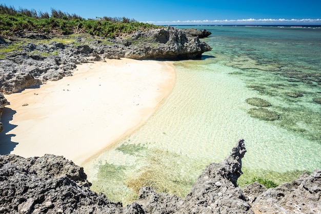 Gemütlicher versteckter Strand mit weißem Sand, umgeben von Felsen, smaragdgrünem Meer voller Korallenriffe