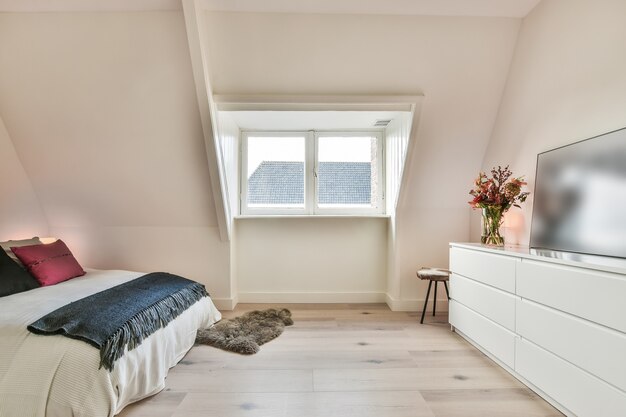 Gemütliches Bett in der Ecke eines modernen Schlafzimmers im minimalistischen Stil mit weißen Wänden und flauschigen Teppichen auf Holzboden und mit farbenfroher Beleuchtung