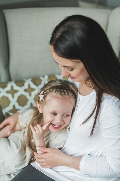 Gemütliches Heimporträt einer jungen schönen dunkelhaarigen Mutter und ihrer 4-jährigen Tochter mit langen glänzenden Haaren Familienbeziehungen Liebe