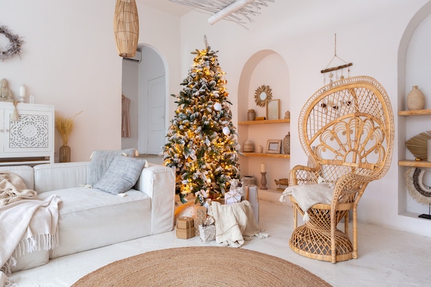 Gemütliches Interieur eines hellen Apartments im balinesischen Stil mit komplett weißen Wänden und Korbmöbeln. Wohnzimmer voller Tageslicht mit Weihnachtsbaum geschmückt