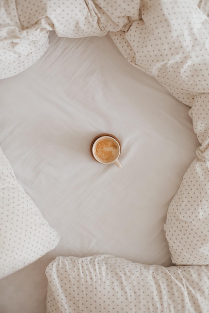 Gemütliches, ungemachtes, unordentliches Bett mit einer Kaffeetasse am Morgenfrühstück im Bett