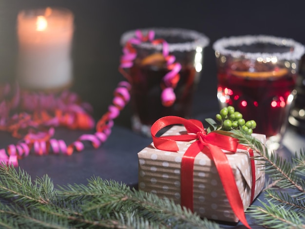 Gemütliches, warmes Weihnachtsdekor, Weihnachtsstimmung und festliche Stimmung, eingewickeltes Geschenk mit rotem Band auf dunklem Hintergrund, Glühwein und Neujahrsschmuck aus Tannenkerze und Serpentin