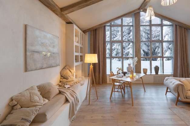 Gemütliches, warmes Wohninterieur eines schicken Landhauses mit einem riesigen Panoramafenster mit Blick auf den Winterwald, offener Holzdekoration, warmen Farben und einem Familienherd