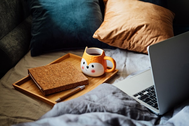 Gemütliches Zuhause Herbst warme Stimmung Laptop Notebook und Tasse Tee am Tablett auf der Decke im Bett im Innenraum