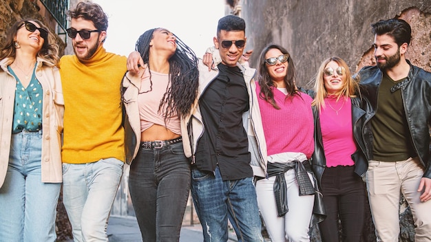 Foto gen z jóvenes interraciales positivos divirtiéndose caminando en la calle con las manos sobre los hombros.