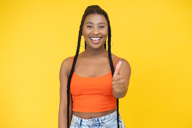 Genehmigungsgeste Zeichen zustimmen Ausgezeichnete Idee Fröhlich lächelnde Afrikanerin zeigt Daumen nach oben Erfolgssymbol isoliert auf orangefarbenem Hintergrund