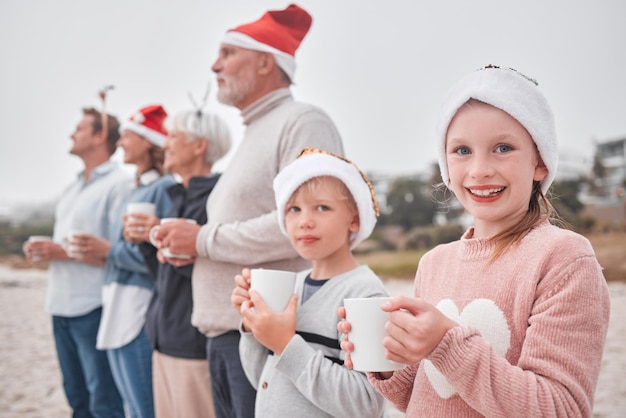 Generaciones familiares y bebidas navideñas y vistas al aire libre durante las vacaciones y el tiempo festivo en la playa Padres, abuelos e hijos felices con una taza de chocolate caliente y un sombrero de Navidad