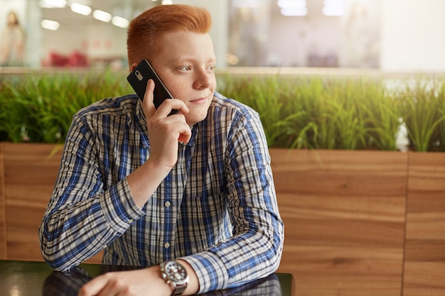 Gengibre jovem bonito falando por telefone