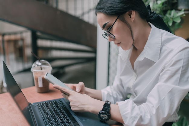 Genial chica asiática sentada trabajando con una laptop en una mesa de madera en la cafetería Gente tailandesa Tiempo para relajarse