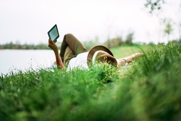 Genießen Sie E-Book in der Nähe des Sees. Mädchen im Gras liegend.