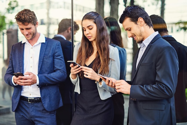 Genießen Sie einige Konnektivität draußen, bevor sie am Seminar teilnehmen. Schnappschuss von Geschäftsleuten, die draußen Mobiltelefone benutzen