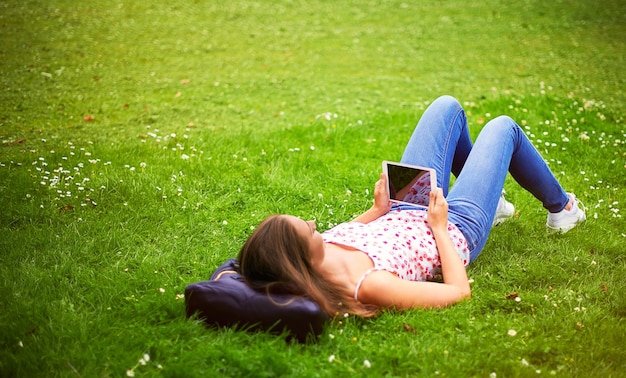 Genießen Sie einige Online-Ablenkungen Aufnahme einer jungen Frau, die ihr digitales Tablet benutzt, während sie im Gras im Park liegt