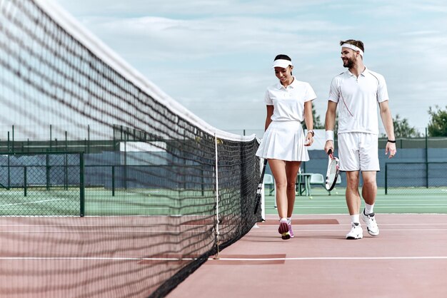 Genießen Sie es, Zeit auf dem Platz zu verbringen, mit einem schönen jungen Paar, das auf dem Tennisplatz spazieren geht